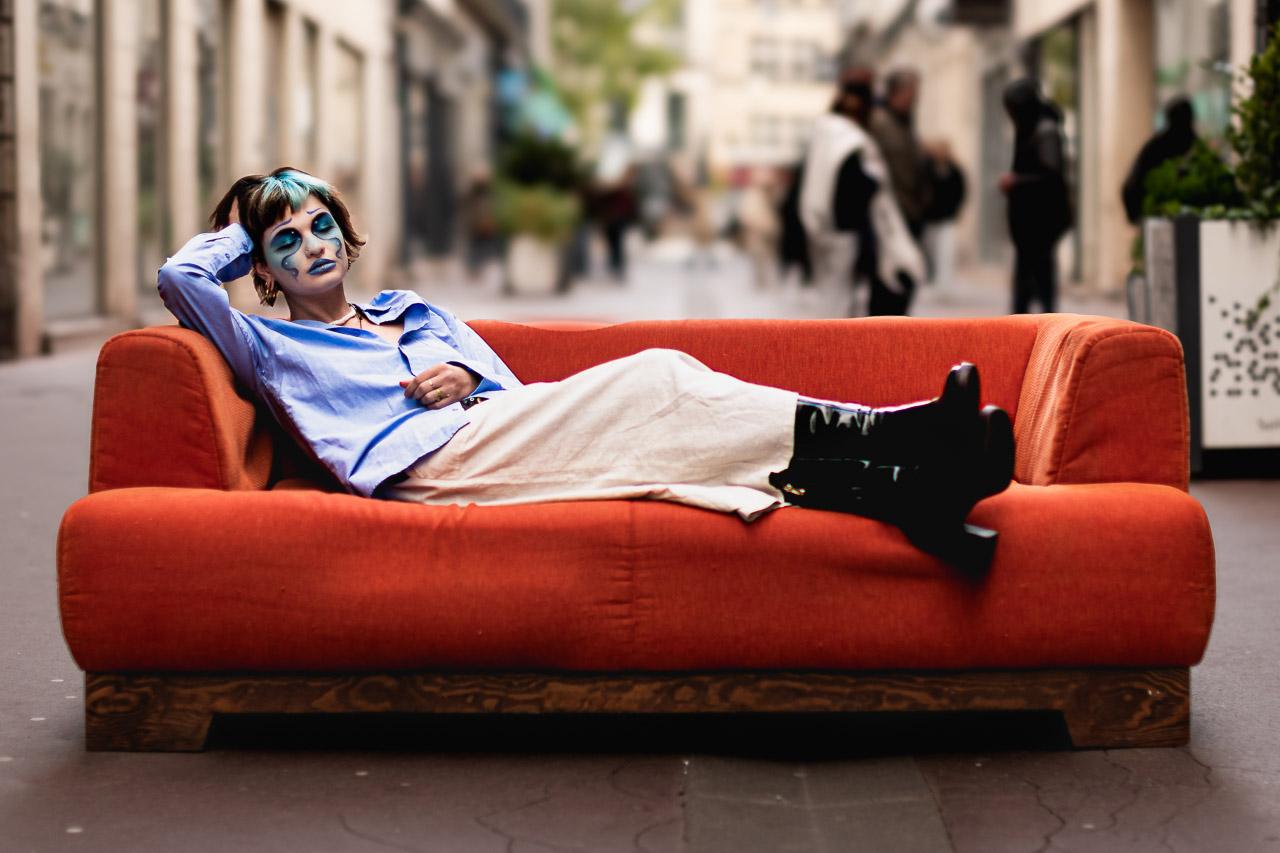 Salon Urbain, un portrait décalé sur canapé orange en pleine rue. Un regard bleu, une mise en scène surprenante et poétique.