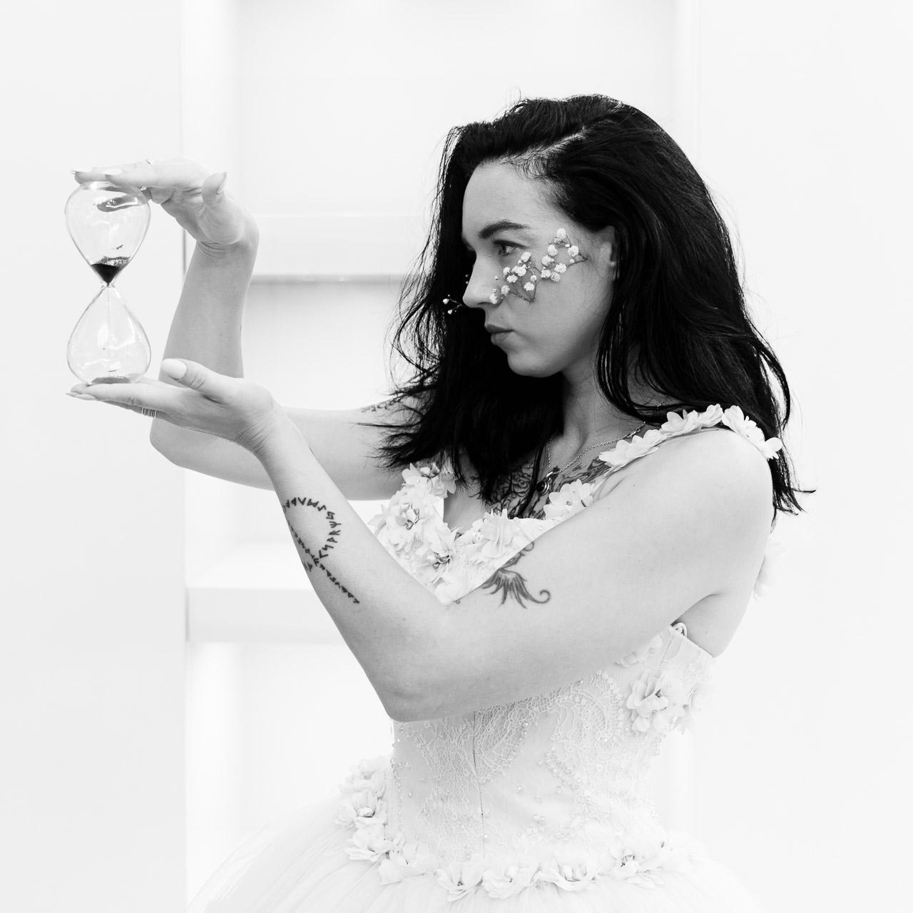 Minute Indocile Portrait artistique en noir et blanc d’une femme tenant un sablier, regard intense et posture concentrée, photographie d’art signée intitulée Minute Indocile.