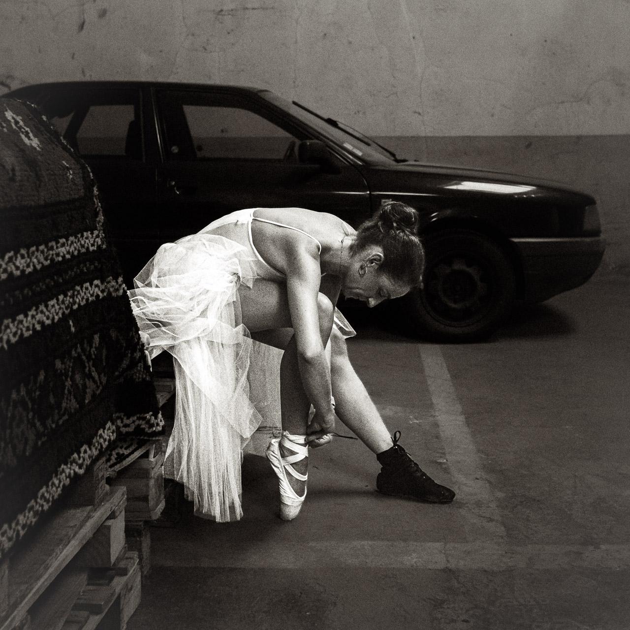 Pas Sage Pas Sage – photographie d’art noir et blanc d’une danseuse en tutu ajustant sa pointe, une chaussure noire à l’autre pied, par Thierry Stentzel