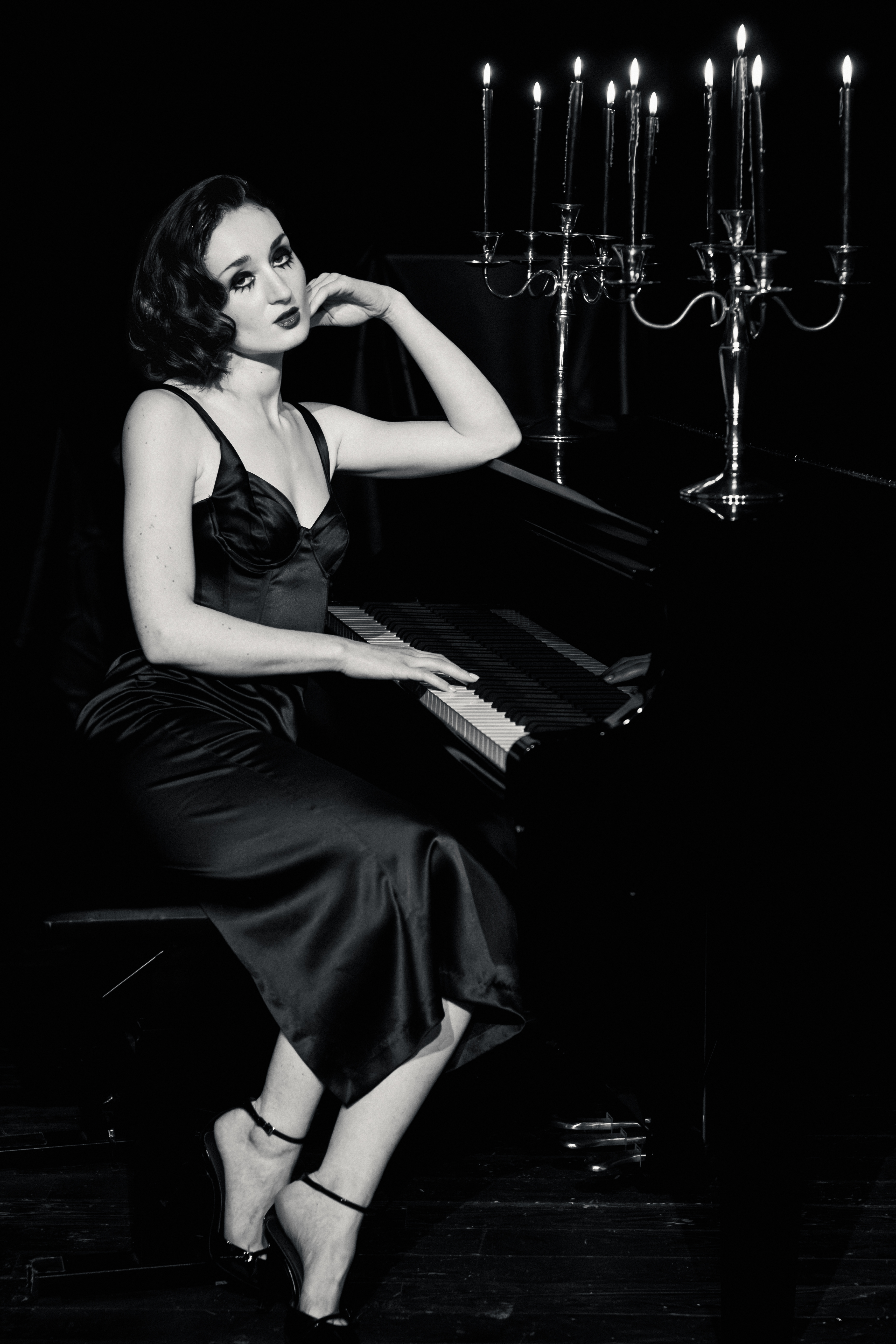 Après Minuit Femme en robe noire assise au piano, éclairée par des chandeliers, photographie noir et blanc